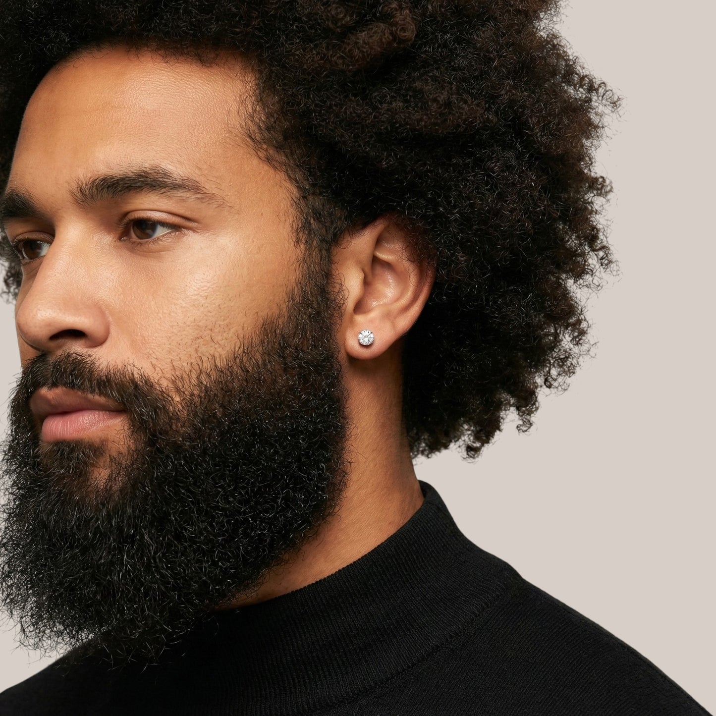 Man with a beard and afro hairstyle wearing a black turtleneck against a neutral background