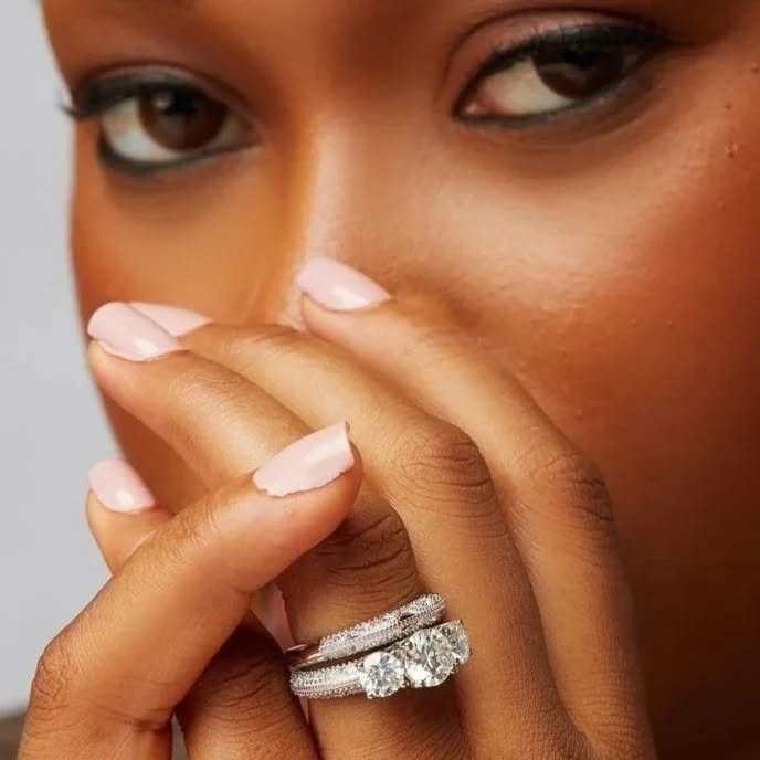 Close-up of a hand with pink nail polish wearing a diamond ring on a neutral background
