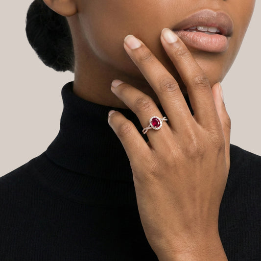 Close-up of a hand wearing a ring with a red gemstone, against a neutral background.