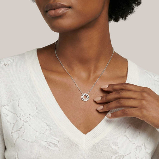 Woman wearing a silver necklace with a circular pendant on a neutral background