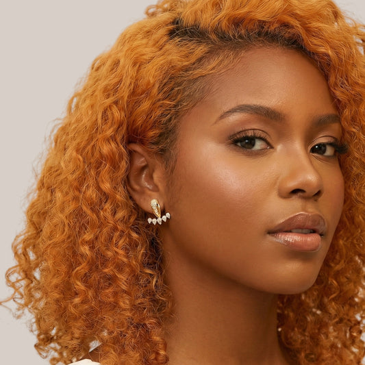 Woman with curly orange hair wearing earrings against a neutral background
