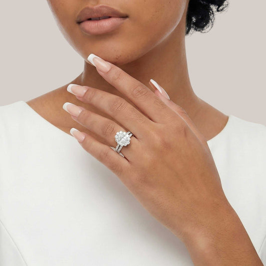 Close-up of a hand wearing a silver ring with a floral design on a neutral background