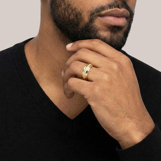 Man wearing a gold ring on his finger with a neutral background