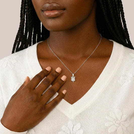 Woman wearing a silver necklace with a pendant, holding her hand to her chest.