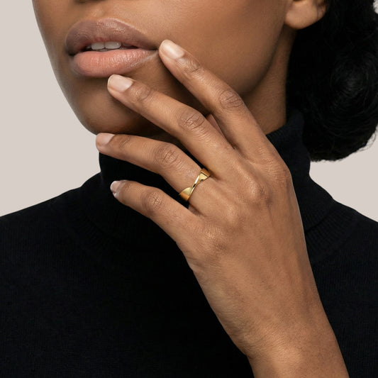 Close-up of a hand wearing a gold ring with a neutral background