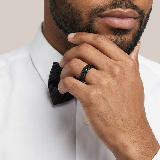 Man wearing a black bow tie and ring, with a neutral background