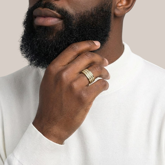 Man wearing a gold ring on his finger, touching his beard against a neutral background
