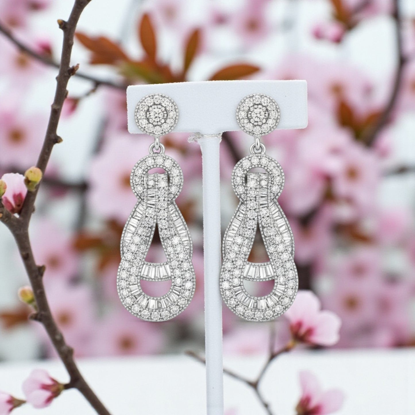 Silver earrings on a white stand with a blurred floral background