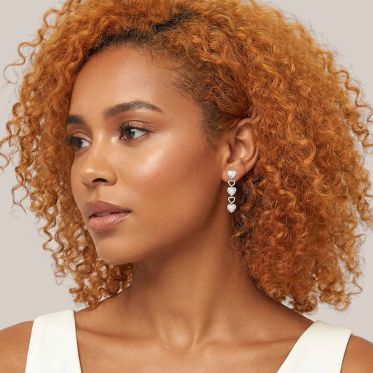 Woman with curly hair wearing heart-shaped earrings against a neutral background