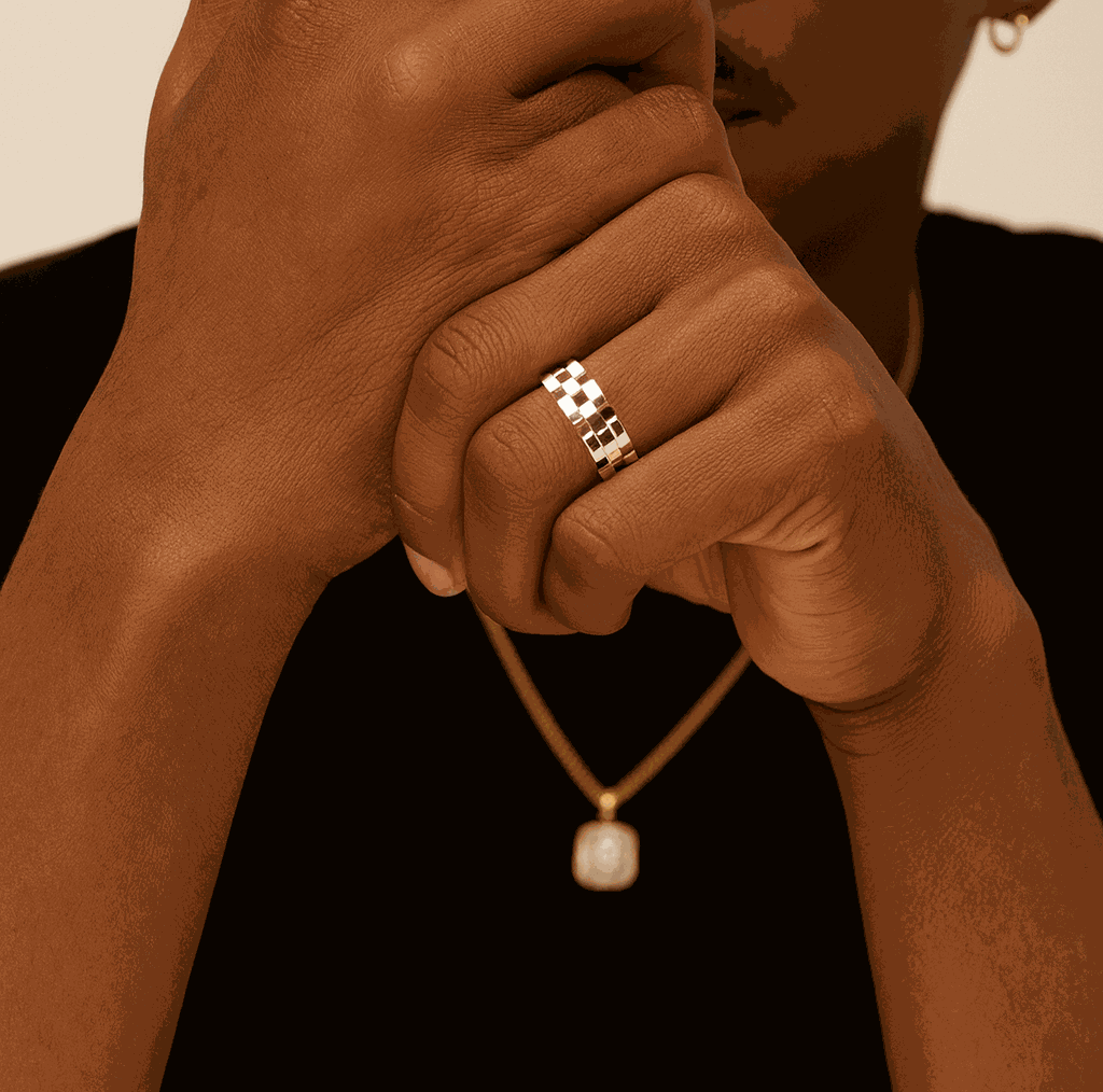 Close-up of a hand wearing a gold ring with a necklace featuring a pearl pendant.