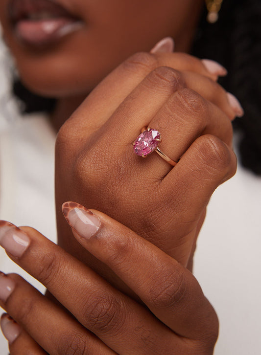 Close-up of a hand wearing a pink gemstone ring against a blurred background