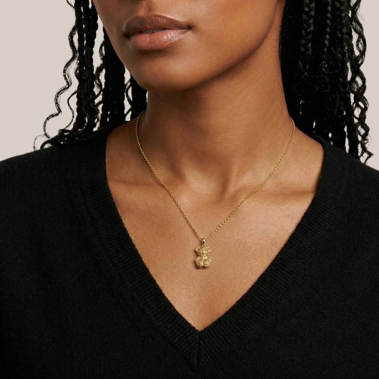 Woman wearing a gold necklace with a pendant against a neutral background