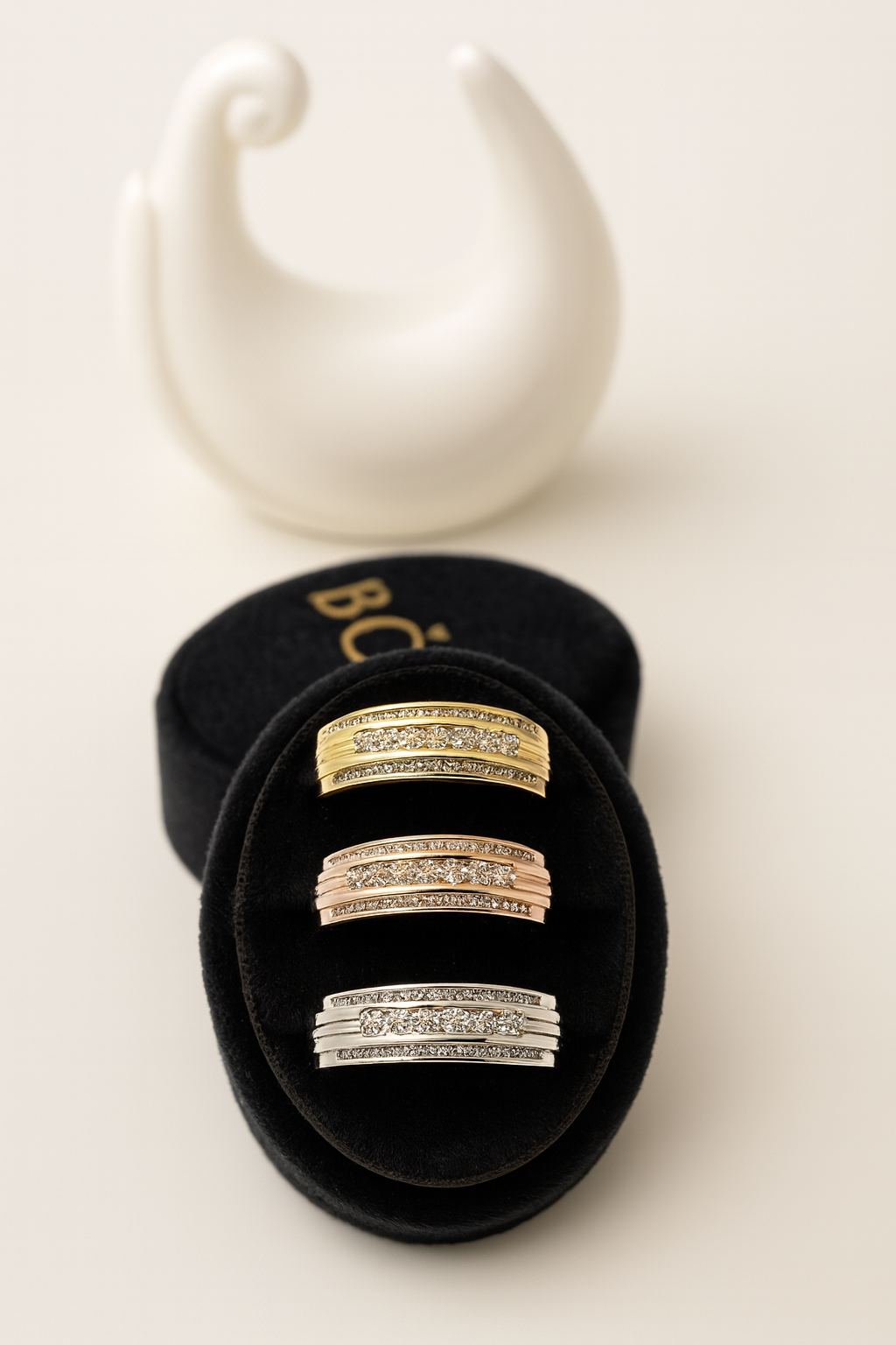 Set of gold and silver rings in a black box with a white swan-shaped holder in the background.