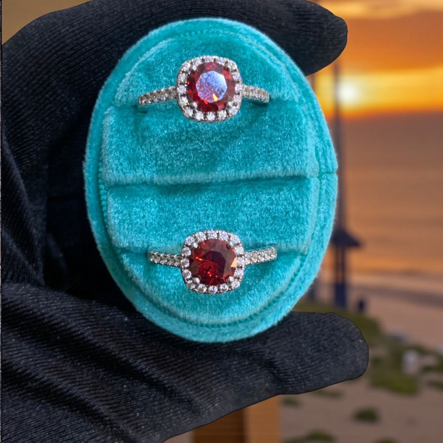 Two diamond rings with red gemstones in a turquoise box held by a gloved hand.