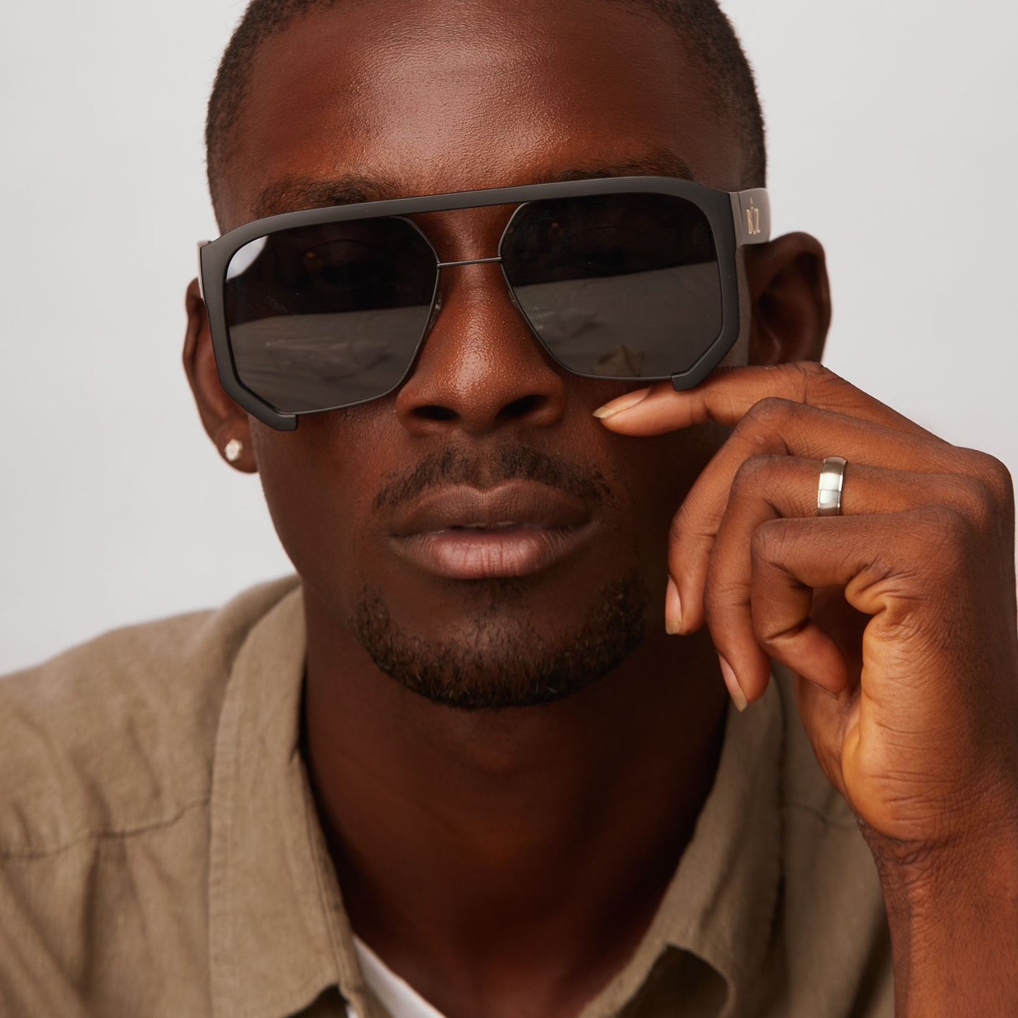 Man wearing sunglasses with one hand on a neutral background