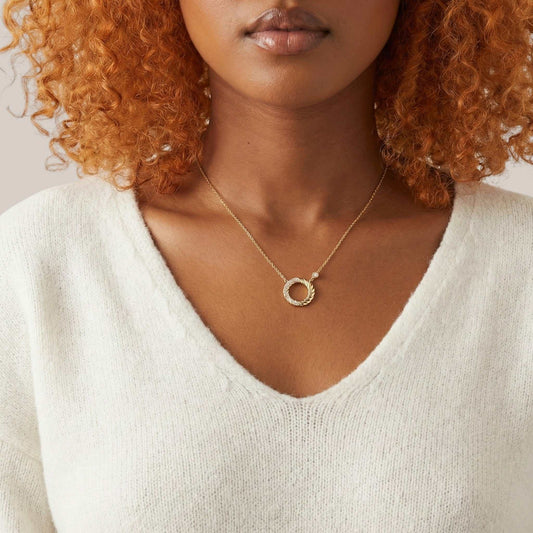 Woman wearing a gold necklace with a circular pendant against a neutral background
