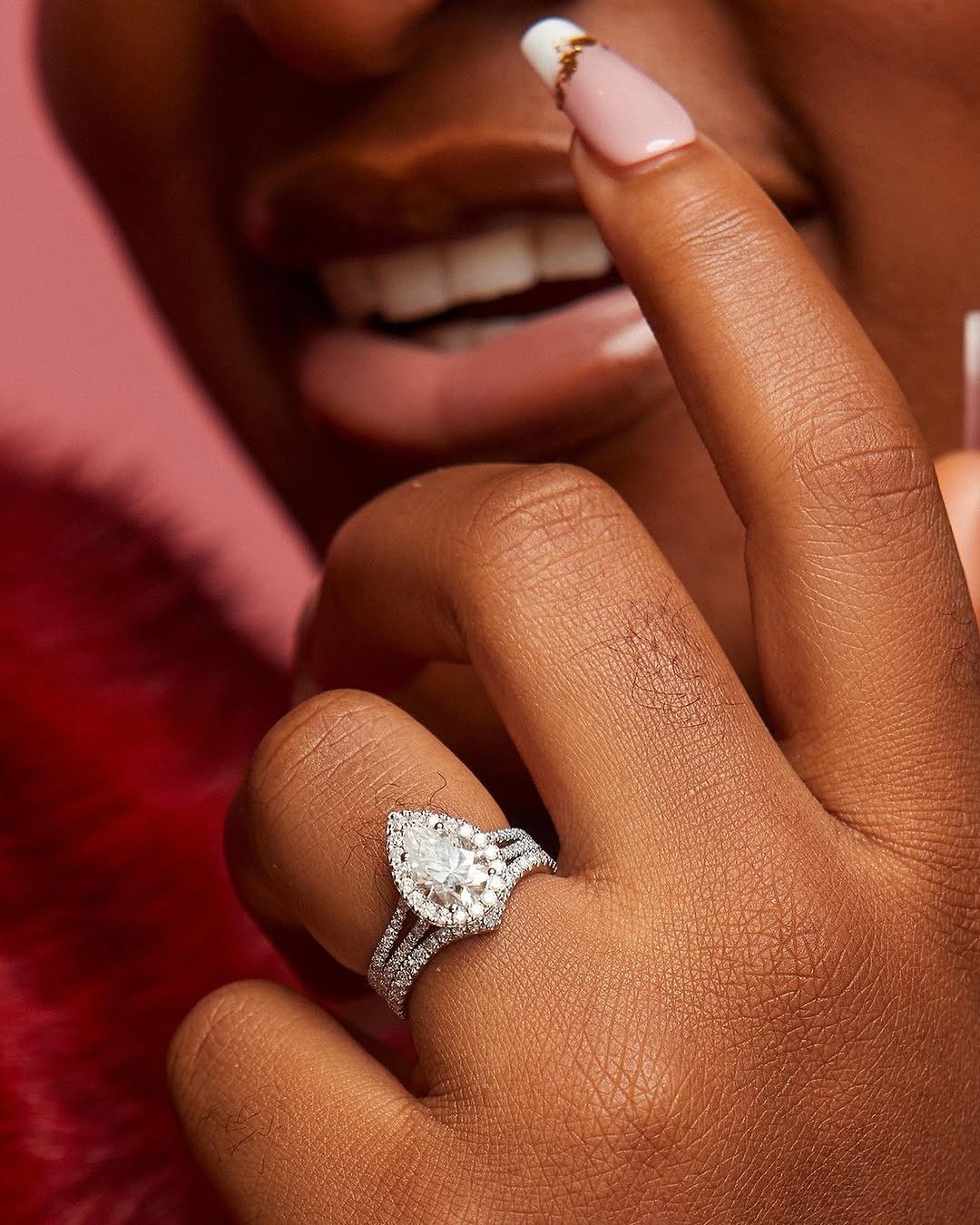 A person's hand displaying a pear-cut moissanite ring set in 18K gold, with a band adorned with natural diamonds.