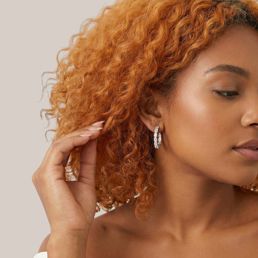Woman with curly hair wearing hoop earrings against a neutral background