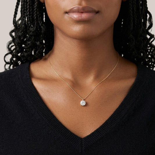 Close-up of a person wearing a gold necklace with a diamond pendant against a neutral background
