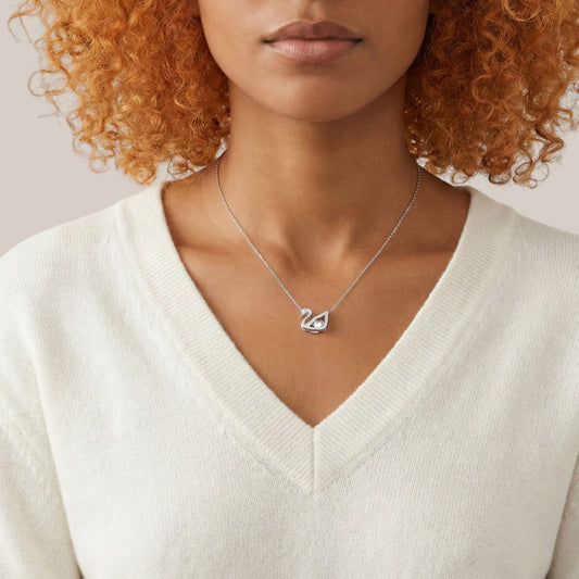 Person wearing a silver necklace with a heart pendant on a neutral background