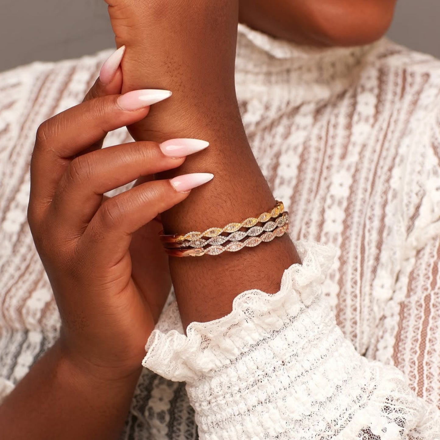 Close-up of a hand wearing two braided bracelets on a textured fabric background
