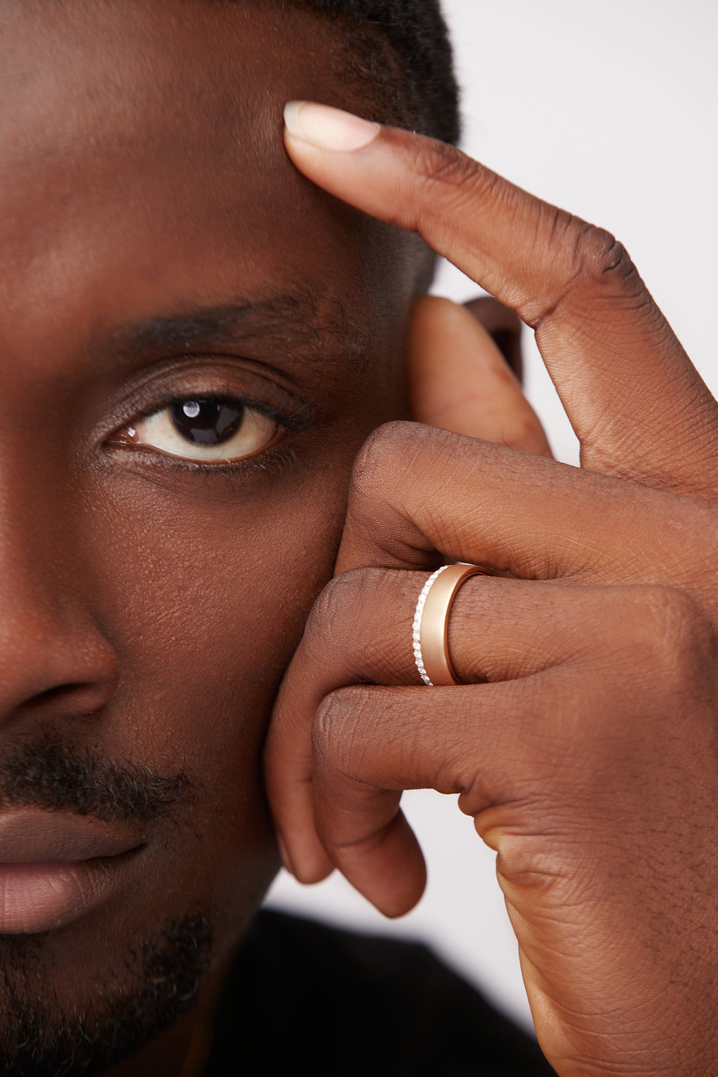 A man's hand featuring a 18K gold ring with natural diamond band on the ring finger.
