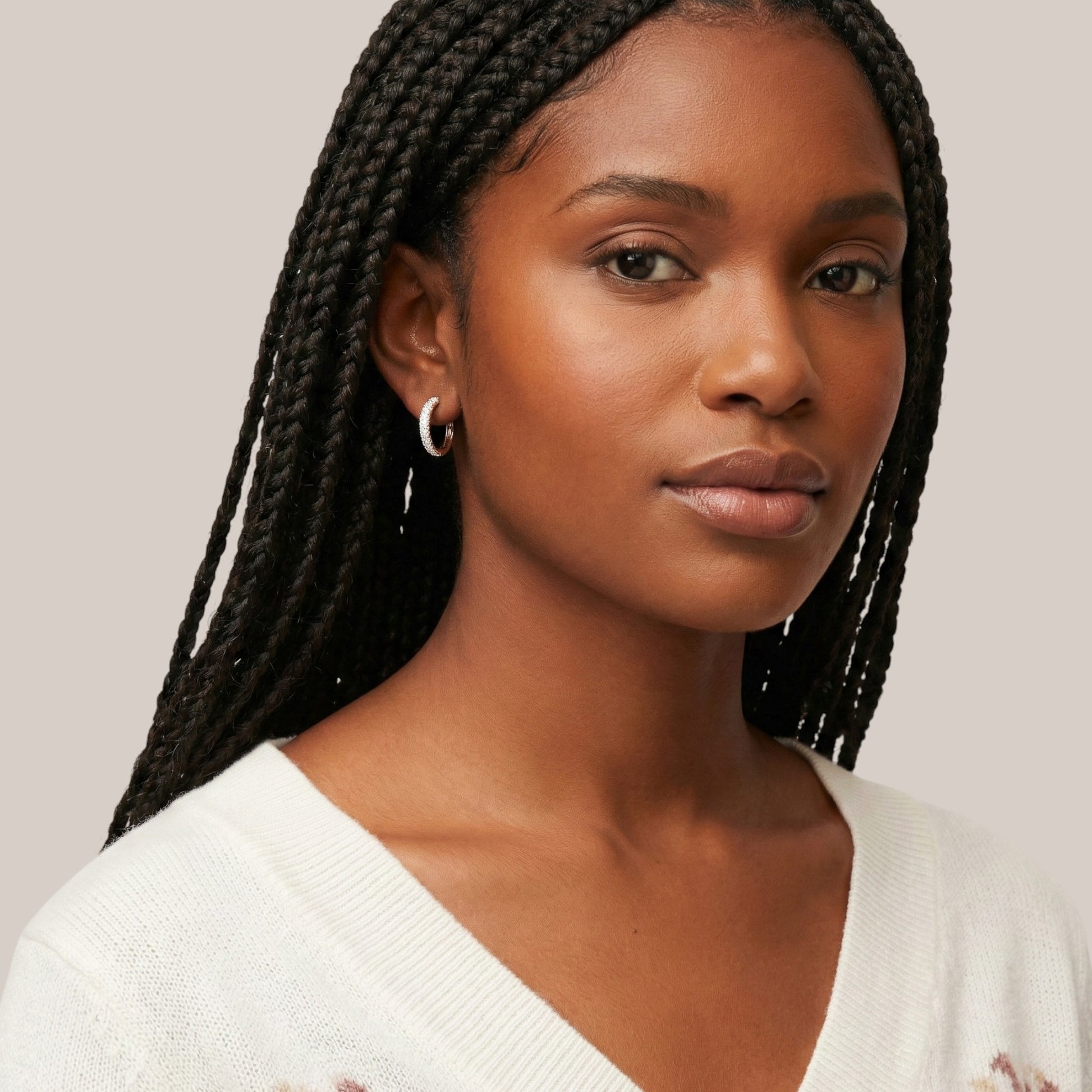 Woman with braided hair wearing a white sweater against a neutral background