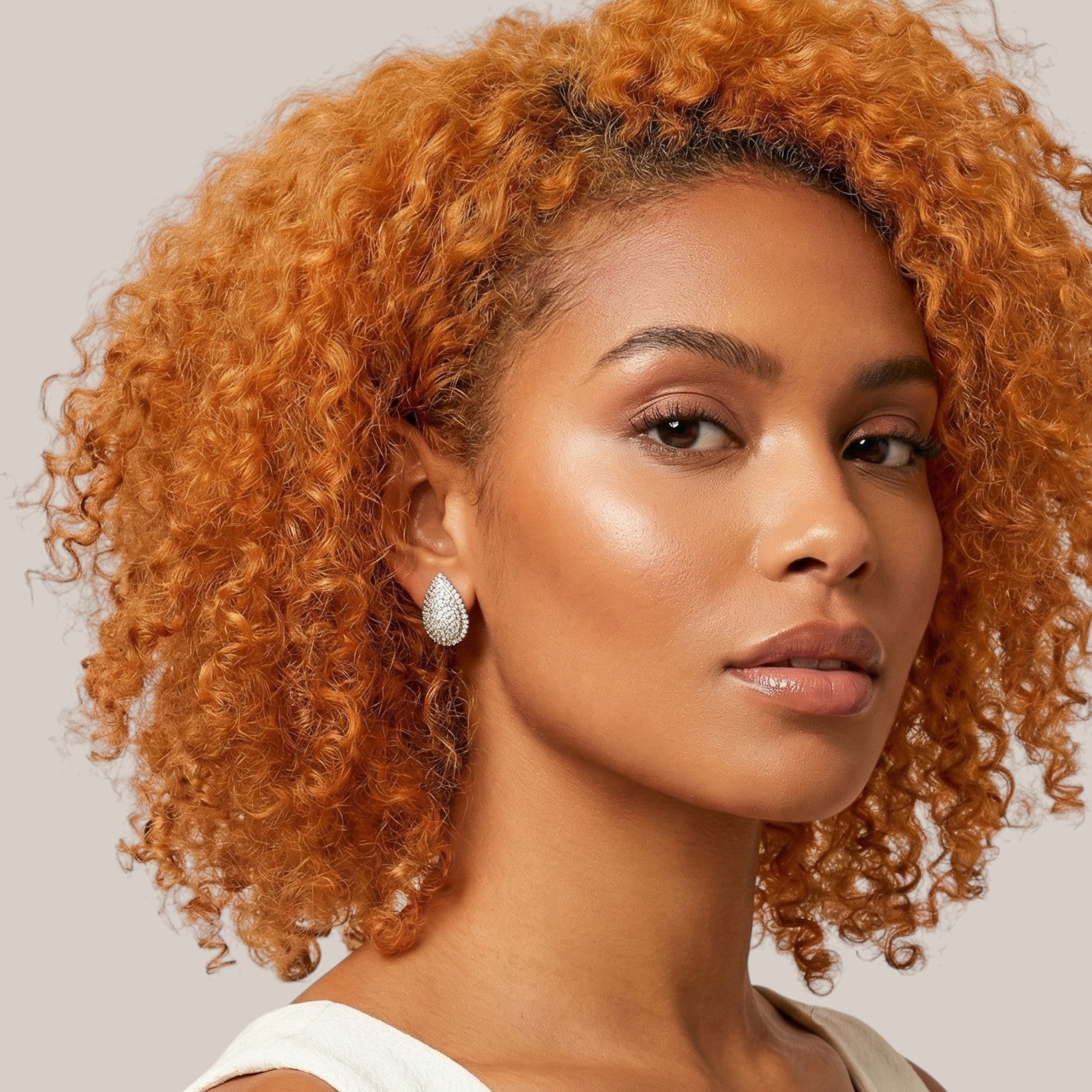 Woman with curly orange hair wearing earrings against a neutral background