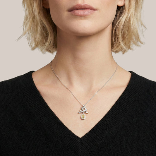 Person wearing a delicate necklace with a small pendant on a plain background