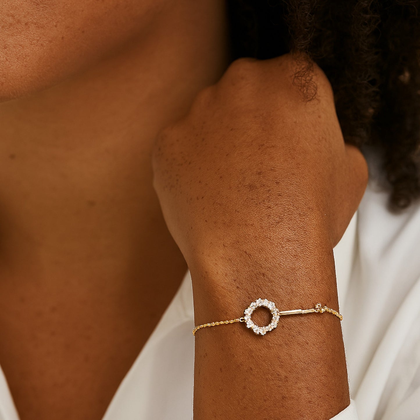 Gold bracelet with a circular design on a wrist against a neutral background