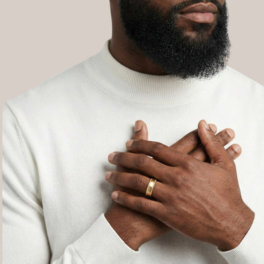 Man wearing a white sweater with his hands clasped in front of him, wearing a gold ring.