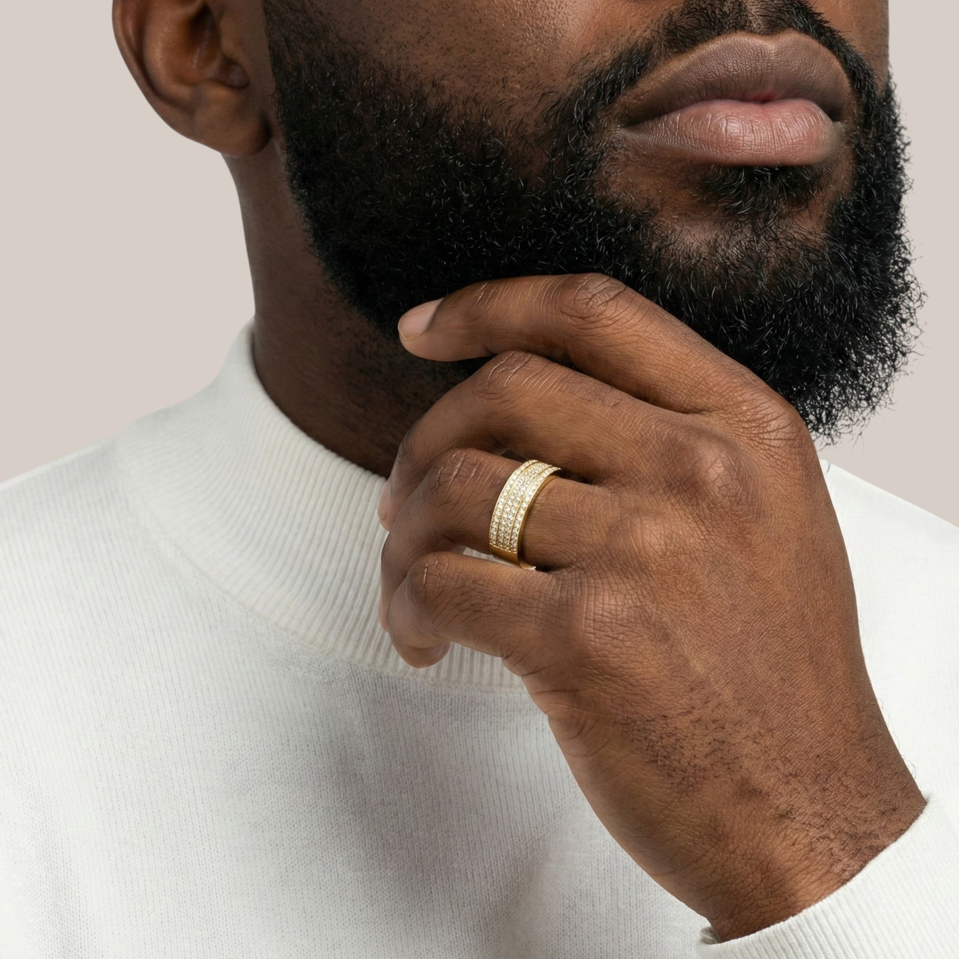 Man wearing a gold ring on his finger, touching his chin against a neutral background