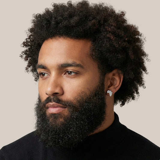 Man with a beard and afro hairstyle wearing a black turtleneck against a neutral background