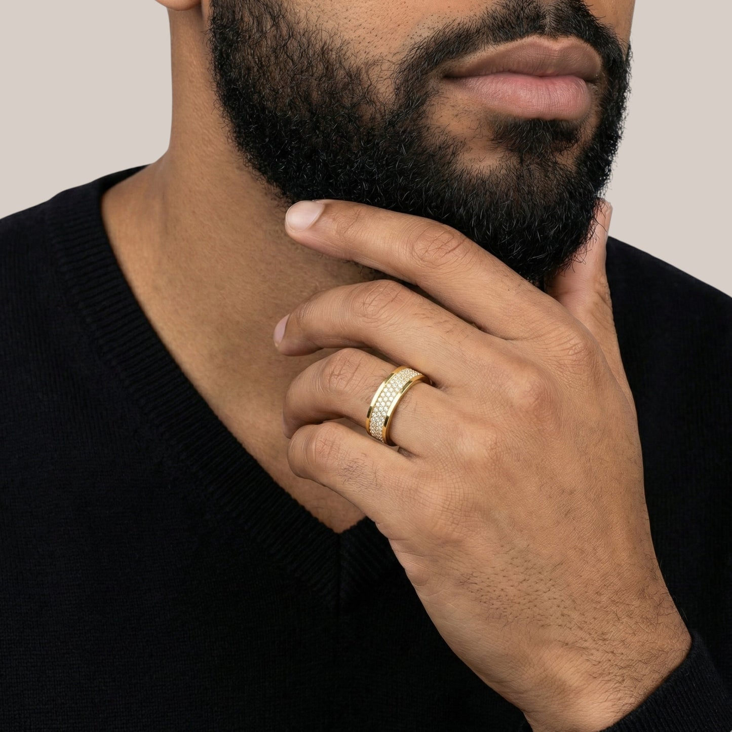 Man wearing a gold ring on his finger, touching his beard against a neutral background
