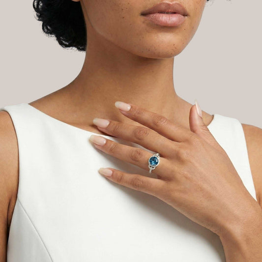 Woman wearing a ring with a blue gemstone on a plain background