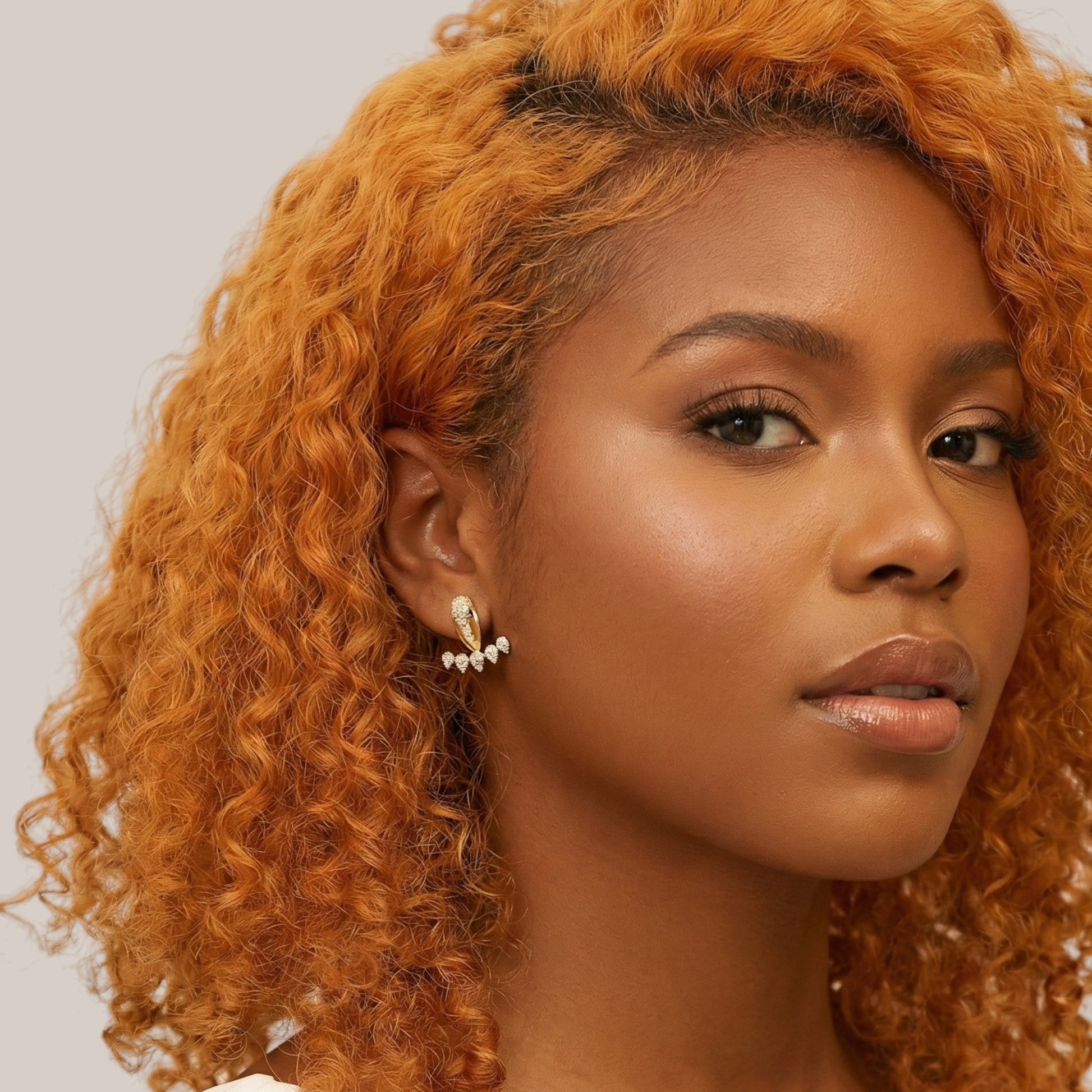 Woman with curly orange hair wearing earrings against a neutral background