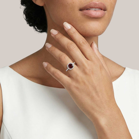 Close-up of a hand wearing a ring with a red gemstone on a neutral background