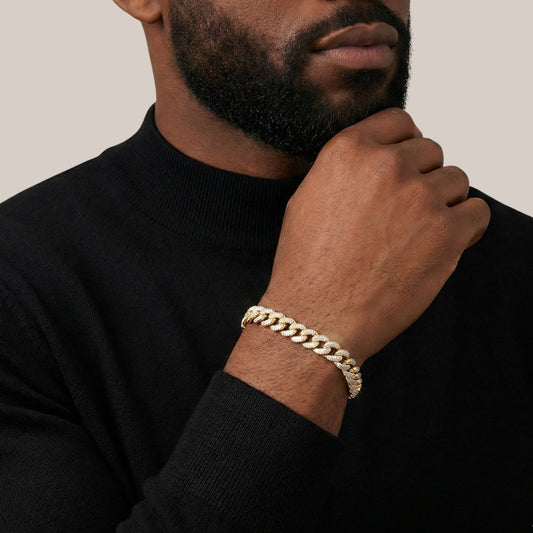 Man wearing a gold chain bracelet on a plain background