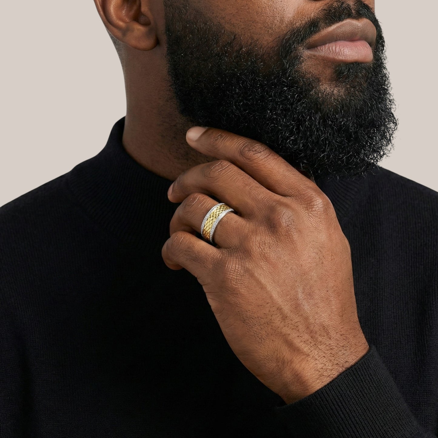 Man with a beard touching his chin, wearing a black sweater and gold rings.
