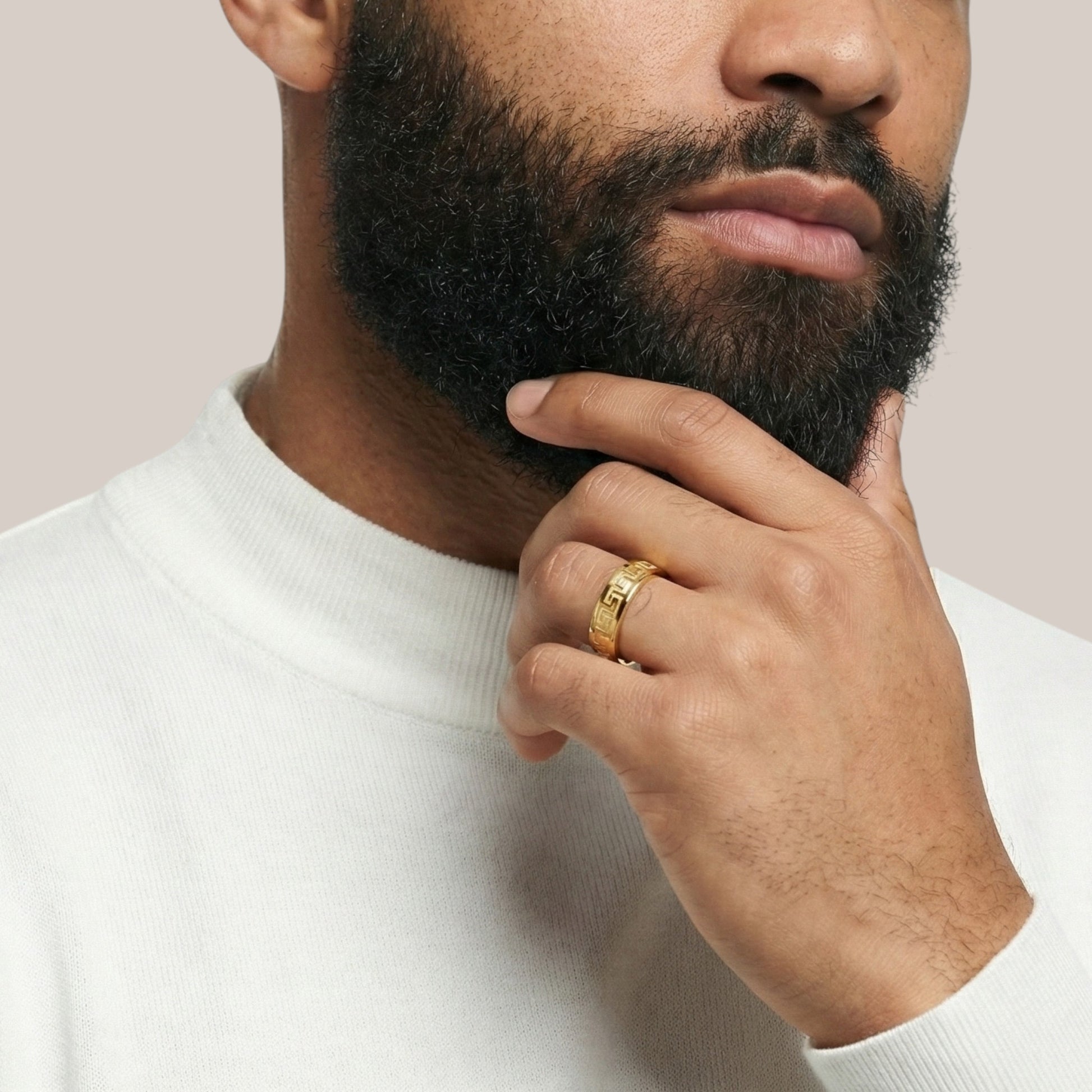 Man wearing a gold ring on his finger, touching his beard against a light background
