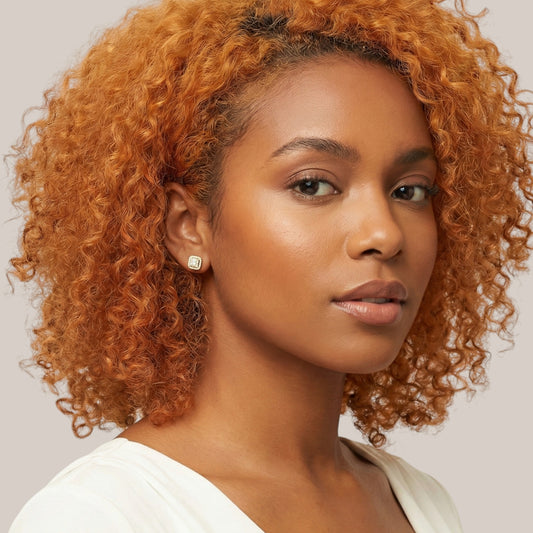 Woman with curly orange hair wearing a white top against a neutral background