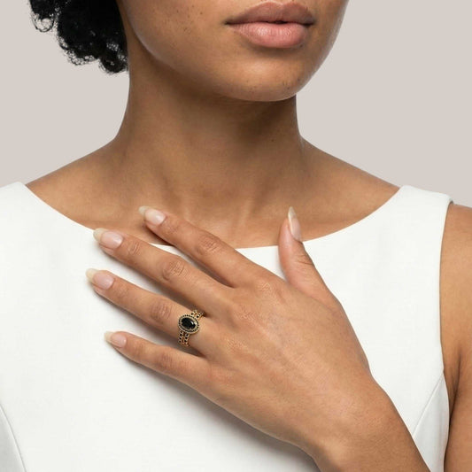 Close-up of a hand wearing a gold ring with a black stone, held against a plain background.