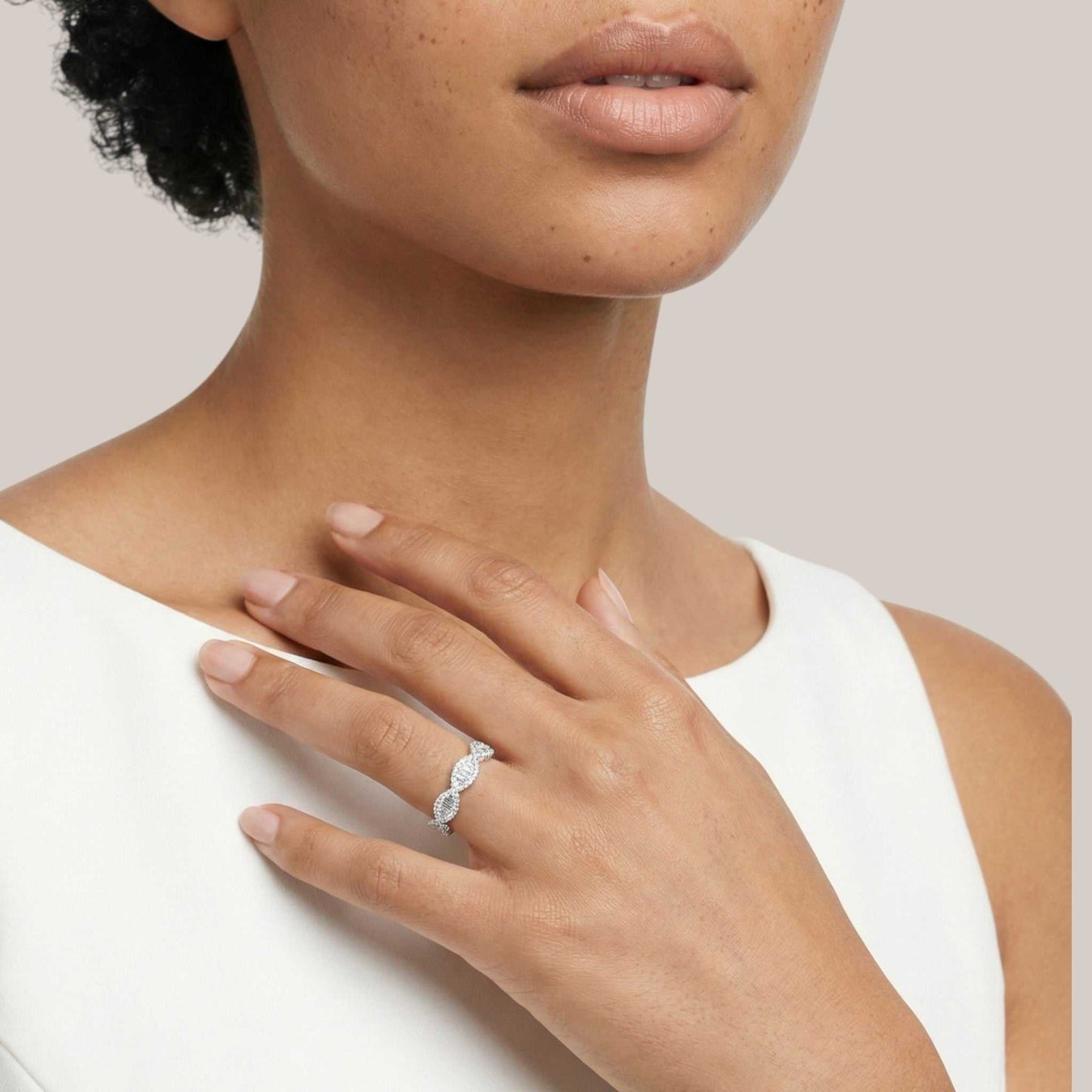 Close-up of a woman's hand wearing a diamond ring on a neutral background