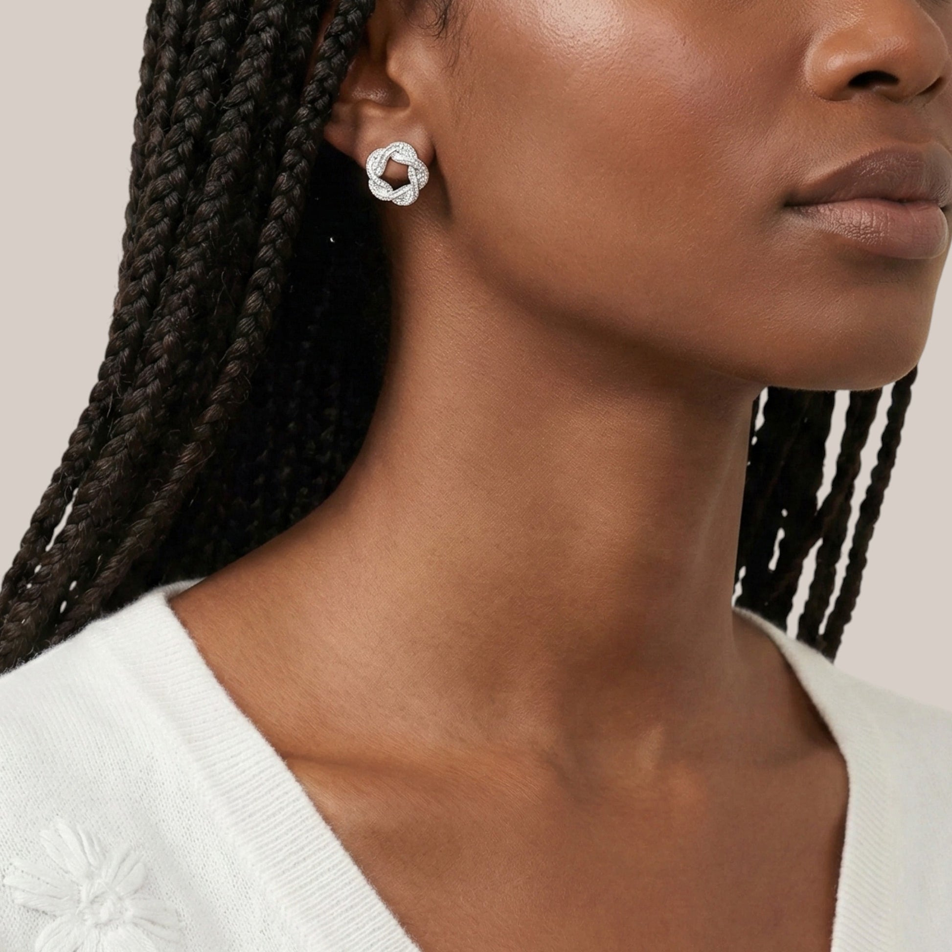 Close-up of a woman wearing a silver earring with braided hair against a neutral background