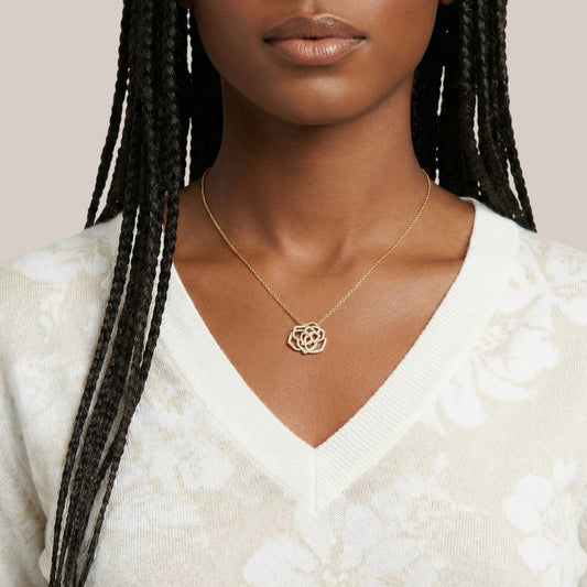 Woman wearing a gold necklace with a white sweater on a neutral background