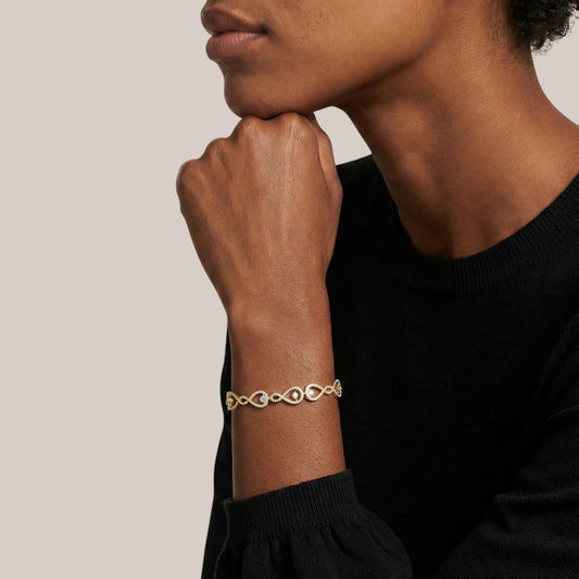 Person wearing a gold bracelet on a neutral background