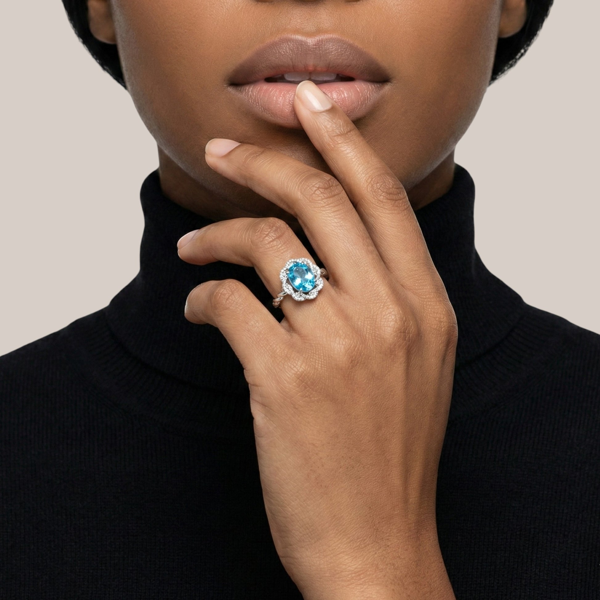 Woman wearing a ring with a blue gemstone on a neutral background