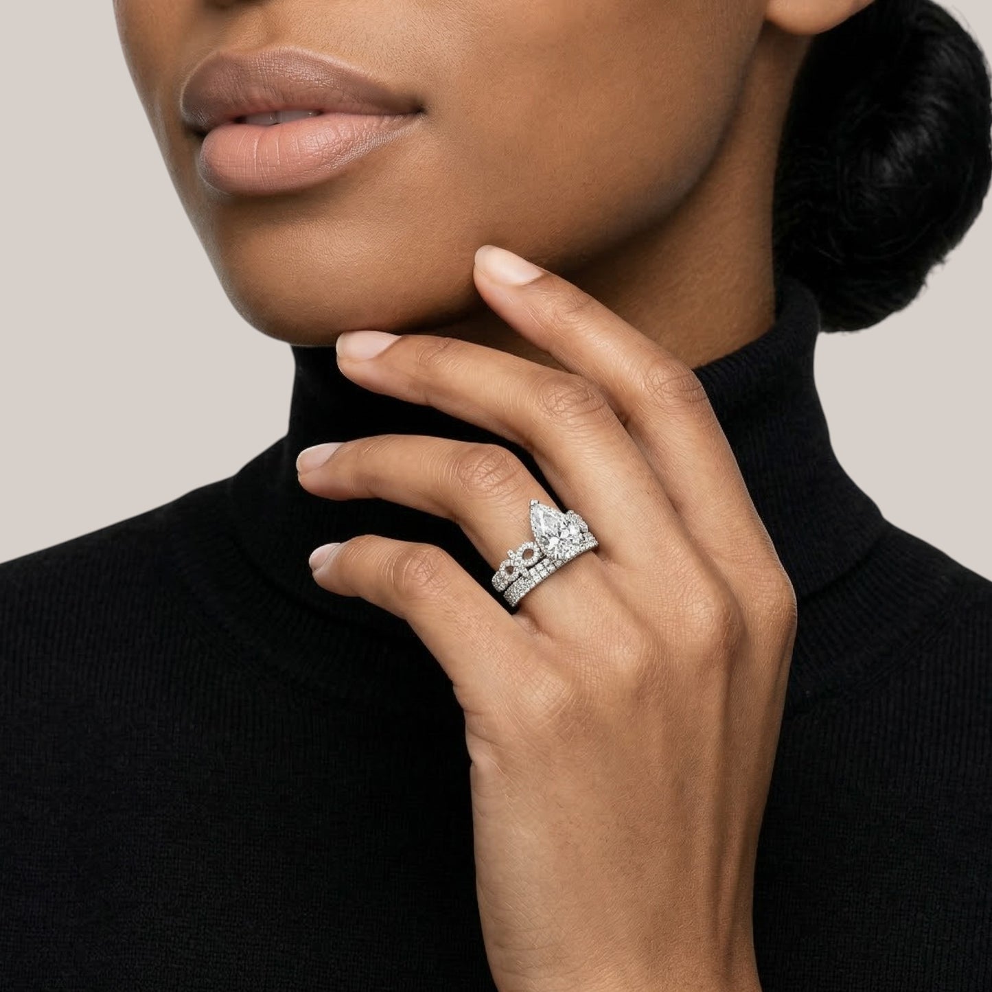 Close-up of a woman's hand wearing a diamond ring with a tiara design on a neutral background