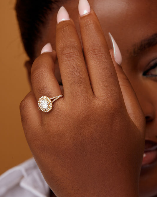 A person showcasing an oval cut moissanite and diamonds engagement ring on their finger.