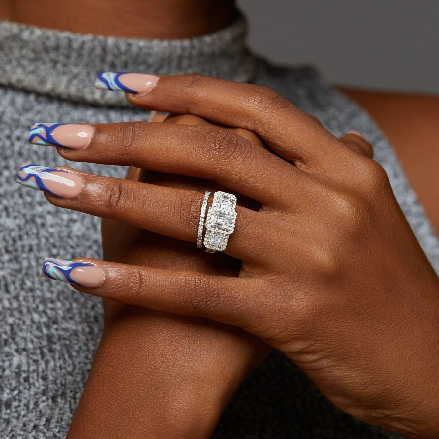 Hand with decorative nails and a diamond ring on a neutral background